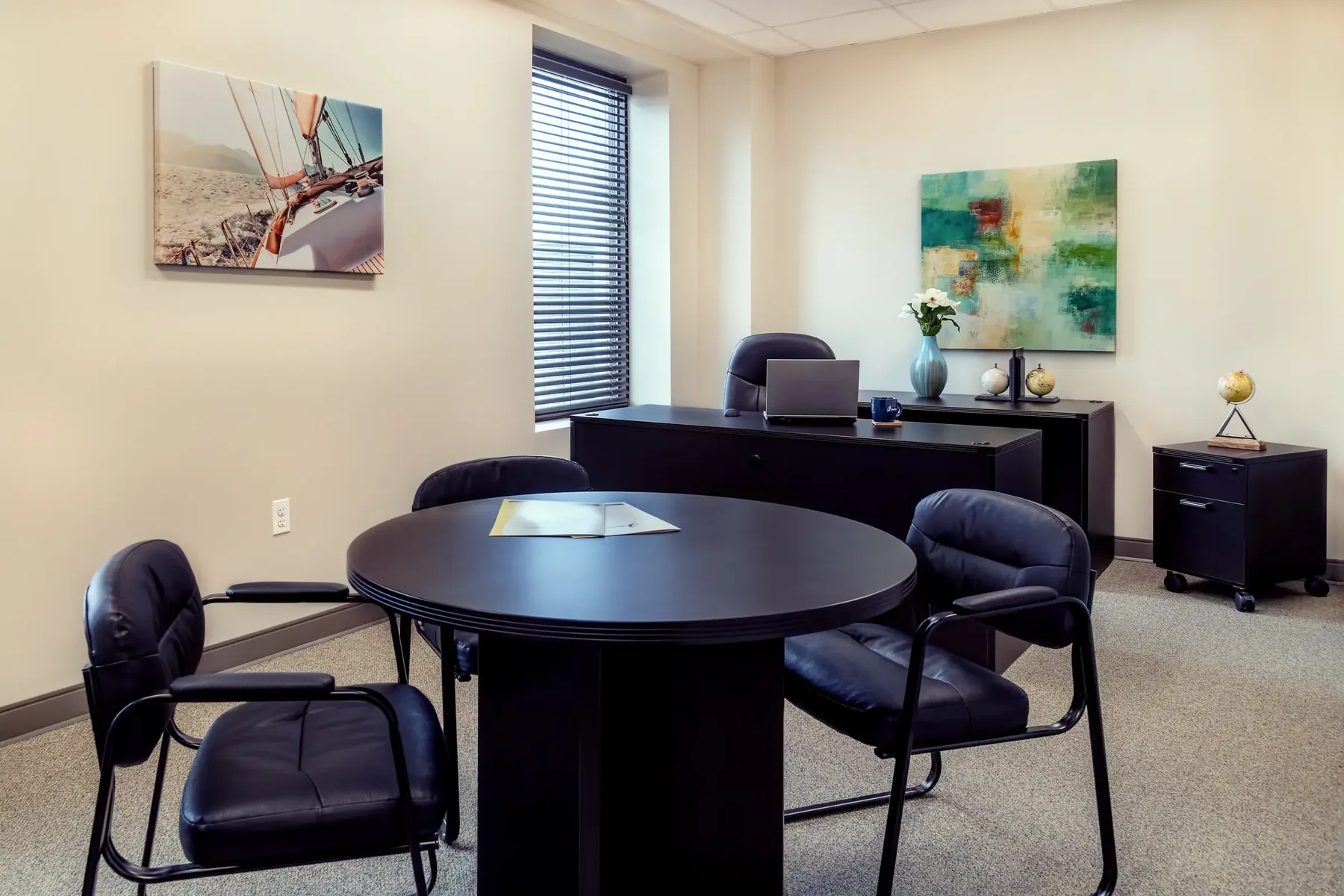 Professional corner office with an executive desk, round meeting table, and modern artwork.
