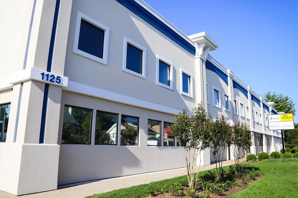 Exterior view of a modern two-story commercial building with light gray walls and bright blue trim on a sunny day.